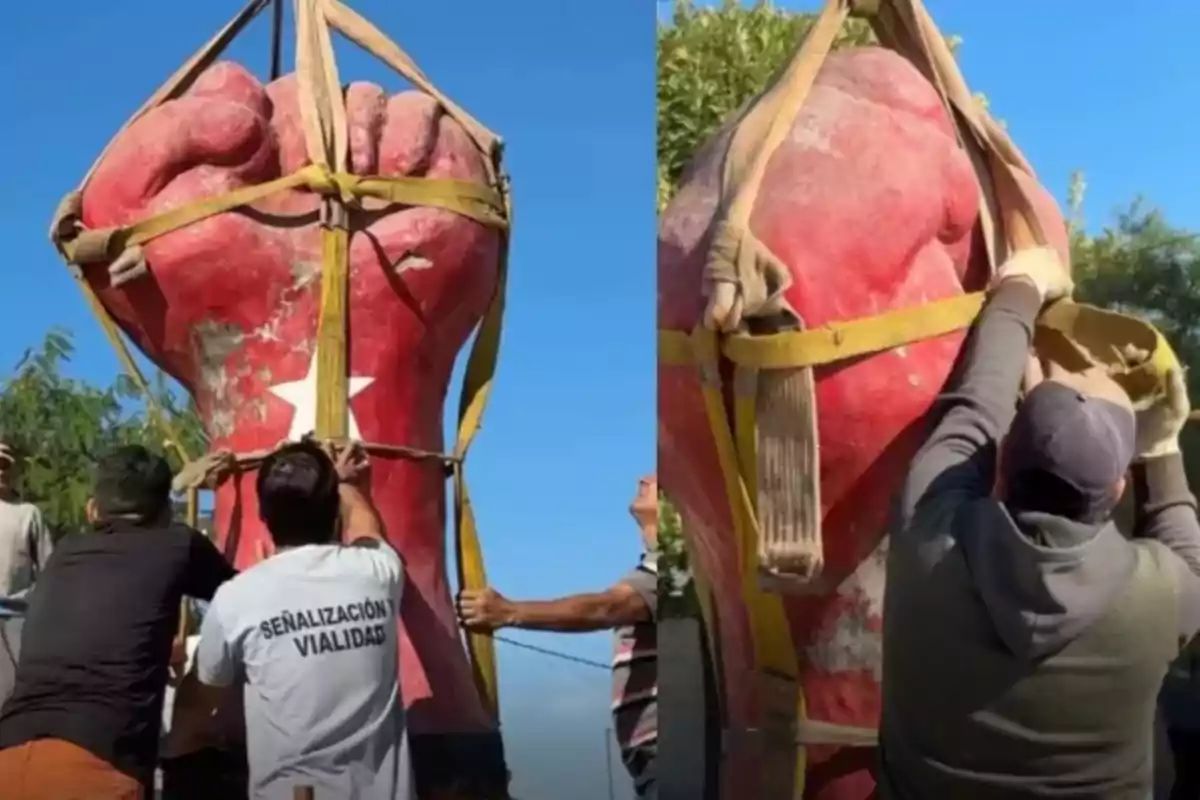 A group of people is working to secure a large sculpture of a red fist with yellow straps.