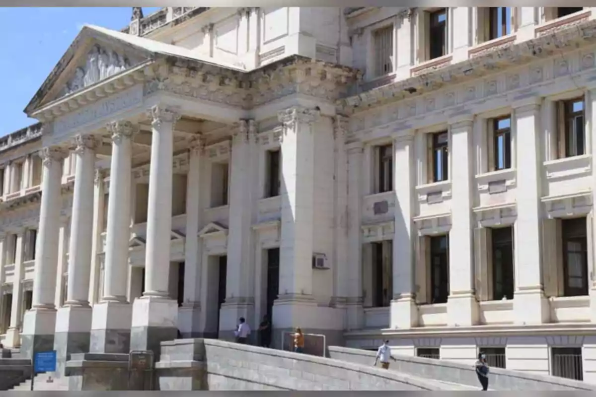 Fachada de un edificio antiguo de estilo neoclásico con columnas y personas caminando por una rampa en la entrada Fachada de un edificio antiguo de estilo neoclásico con columnas y personas caminando por una rampa en la entrada