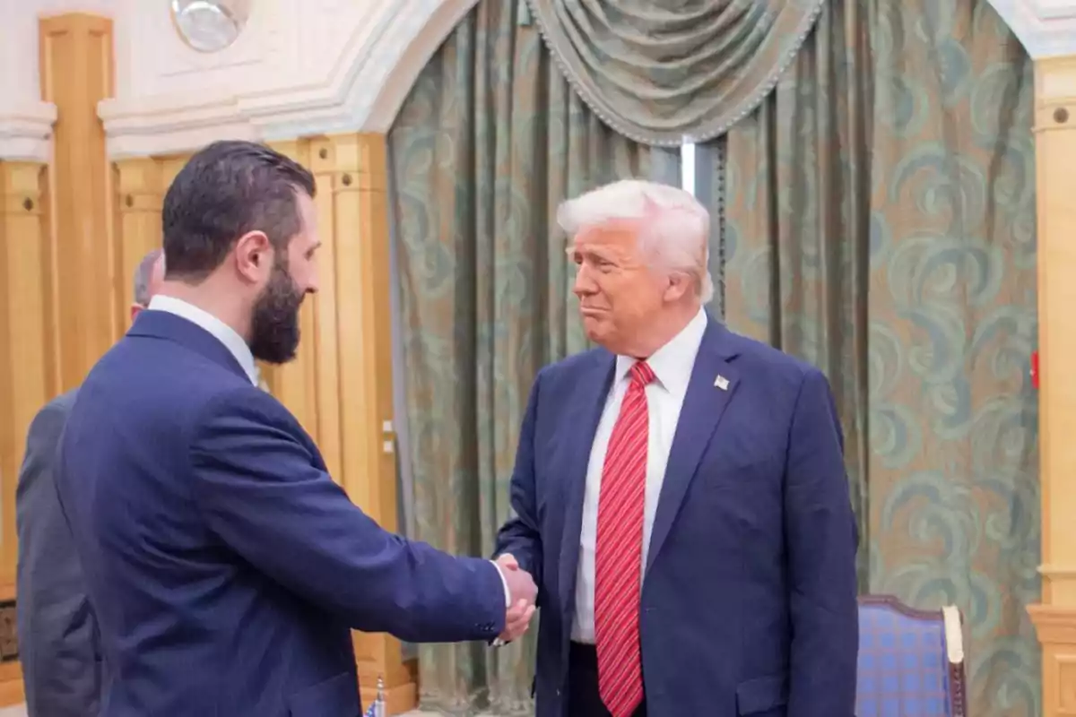 Dos hombres de traje se dan la mano en una sala con cortinas decorativas y muebles elegantes. Dos hombres de traje se dan la mano en una sala con cortinas decorativas y muebles elegantes.