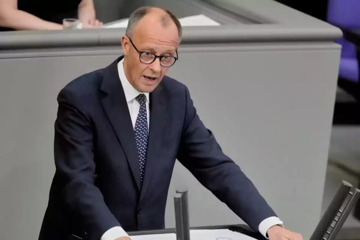A man with glasses and a dark suit speaking at a podium.