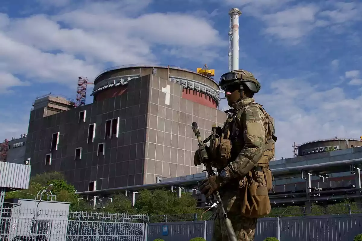 Armed soldier in camouflage uniform and helmet patrolling in front of a nuclear plant under a partly cloudy sky Armed soldier in camouflage uniform and helmet patrolling in front of a nuclear plant under a partly cloudy sky