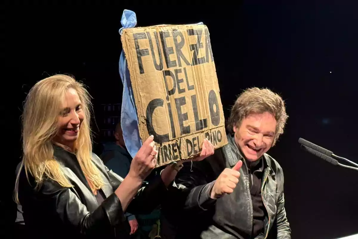 Dos personas sonrientes sostienen un cartel de cartón que dice "Fuerza del Cielo".