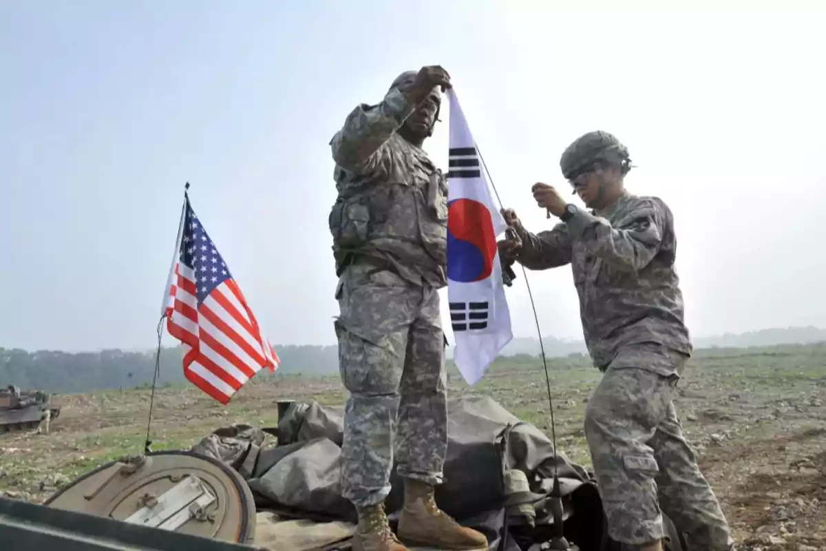 Dos soldados en uniforme militar sostienen una bandera de Corea del Sur junto a una bandera de Estados Unidos en un campo abierto. Dos soldados en uniforme militar sostienen una bandera de Corea del Sur junto a una bandera de Estados Unidos en un campo abierto.