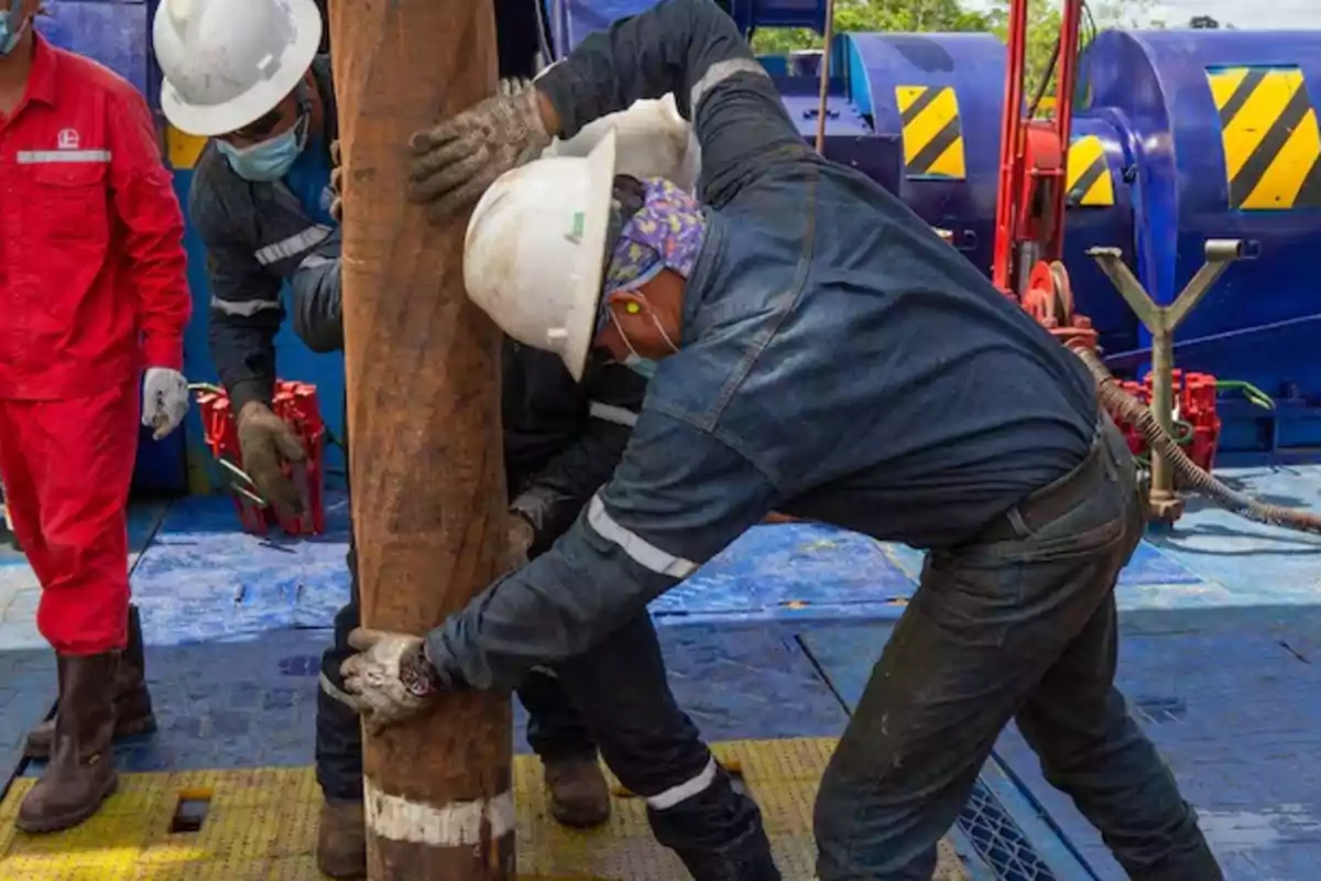 Workers with helmets and protective gear handling a pipe at an industrial site.