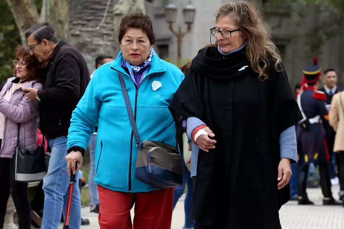 Dos mujeres caminando juntas en un espacio al aire libre rodeadas de otras personas.