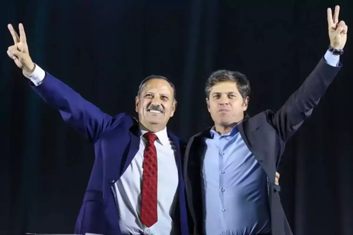 Dos hombres de traje levantando los brazos y haciendo el signo de la victoria con los dedos.