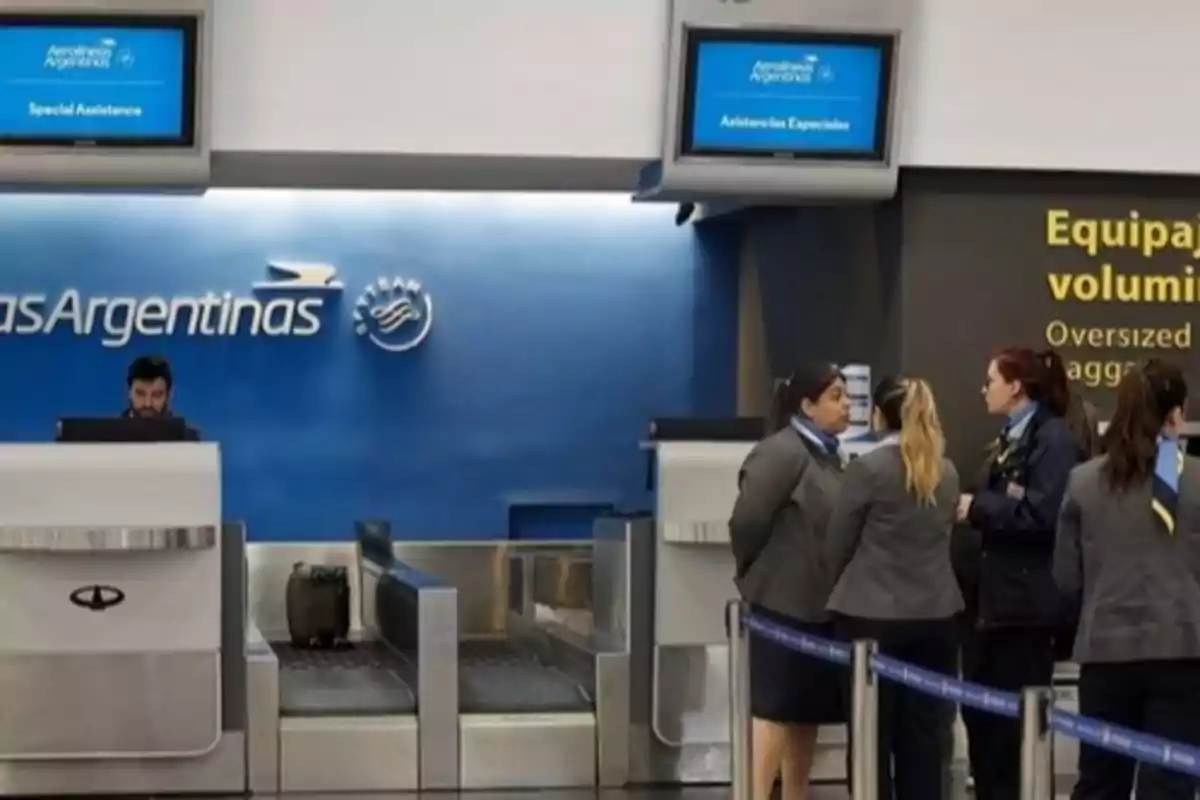 Mostrador de atención al cliente de Aerolíneas Argentinas en un aeropuerto con personal de la aerolínea y pantallas de asistencia especial.