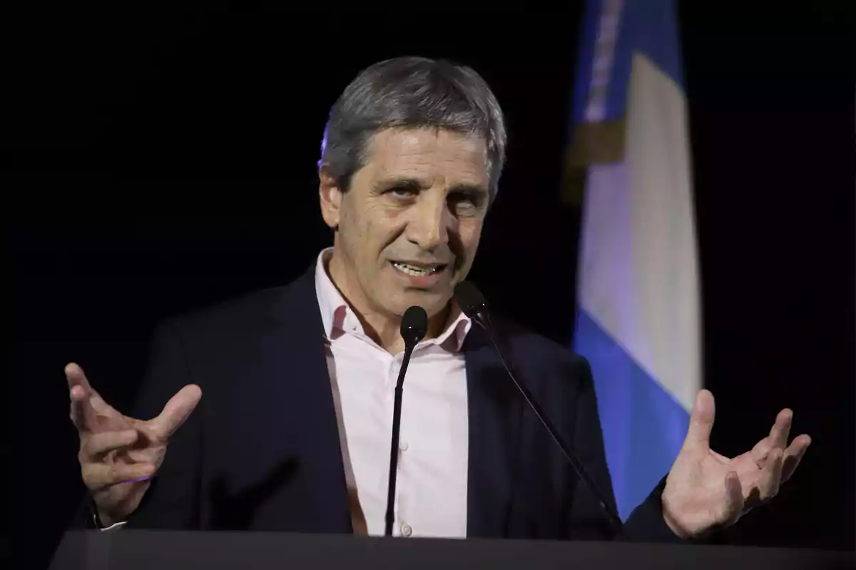 Un hombre hablando en un micrófono con una bandera en el fondo.