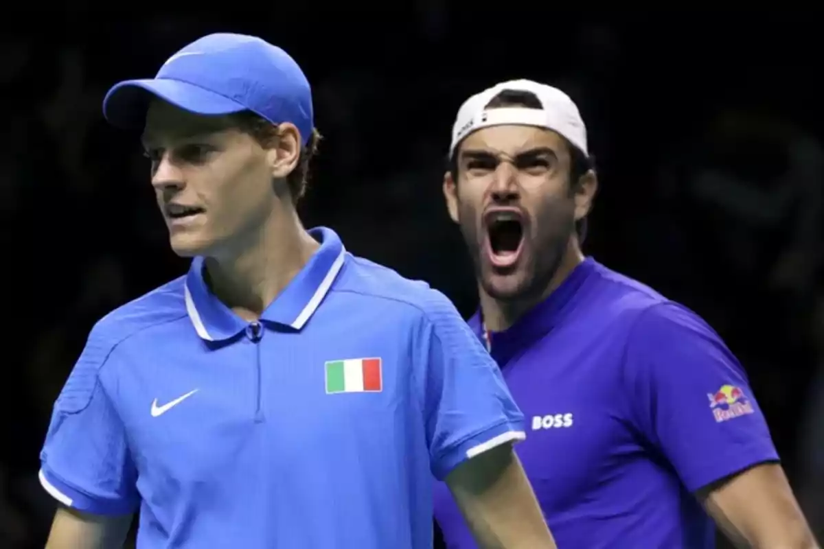 Dos jugadores de tenis con uniformes azules en una cancha durante un partido uno de ellos grita emocionado.