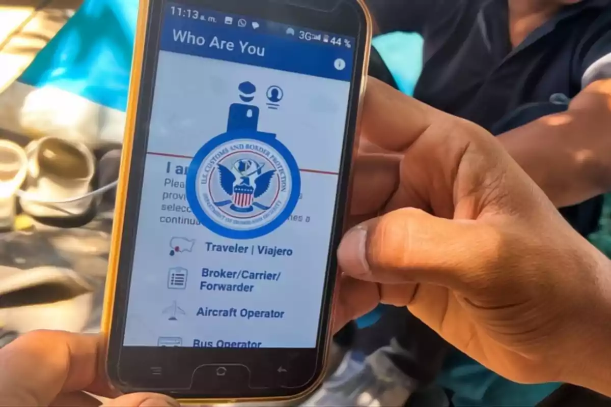 A person holds a mobile phone displaying an app related to U.S. border protection.