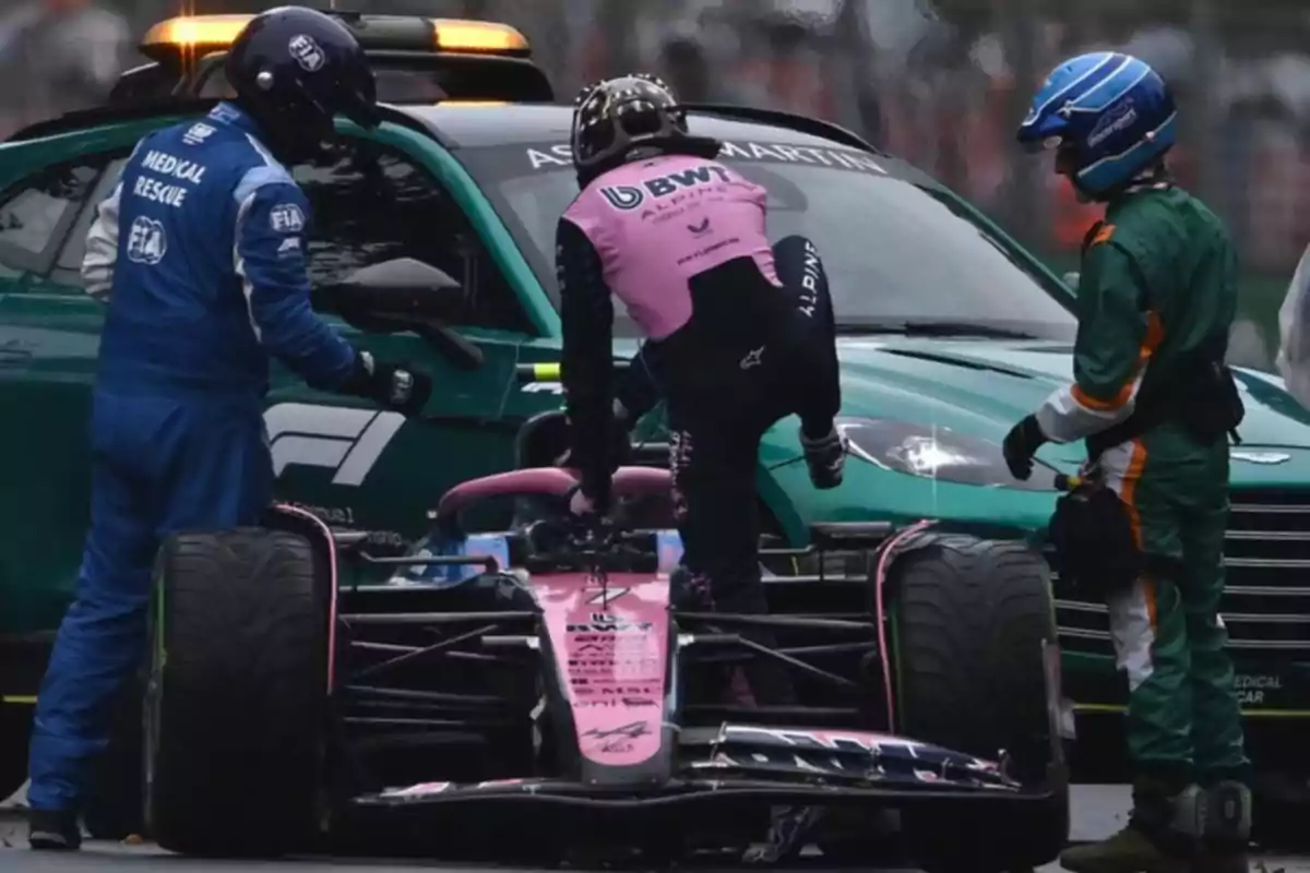 A Formula 1 driver gets out of his pink single-seater while being assisted by rescue personnel and a green medical car. A Formula 1 driver gets out of his pink single-seater while being assisted by rescue personnel and a green medical car.