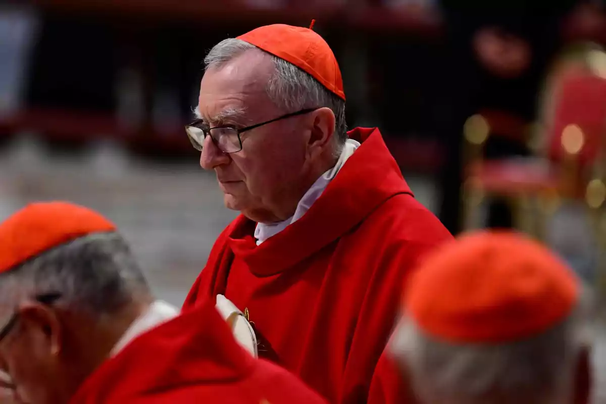 A cardinal in red attire and a matching biretta participates in a religious ceremony.
