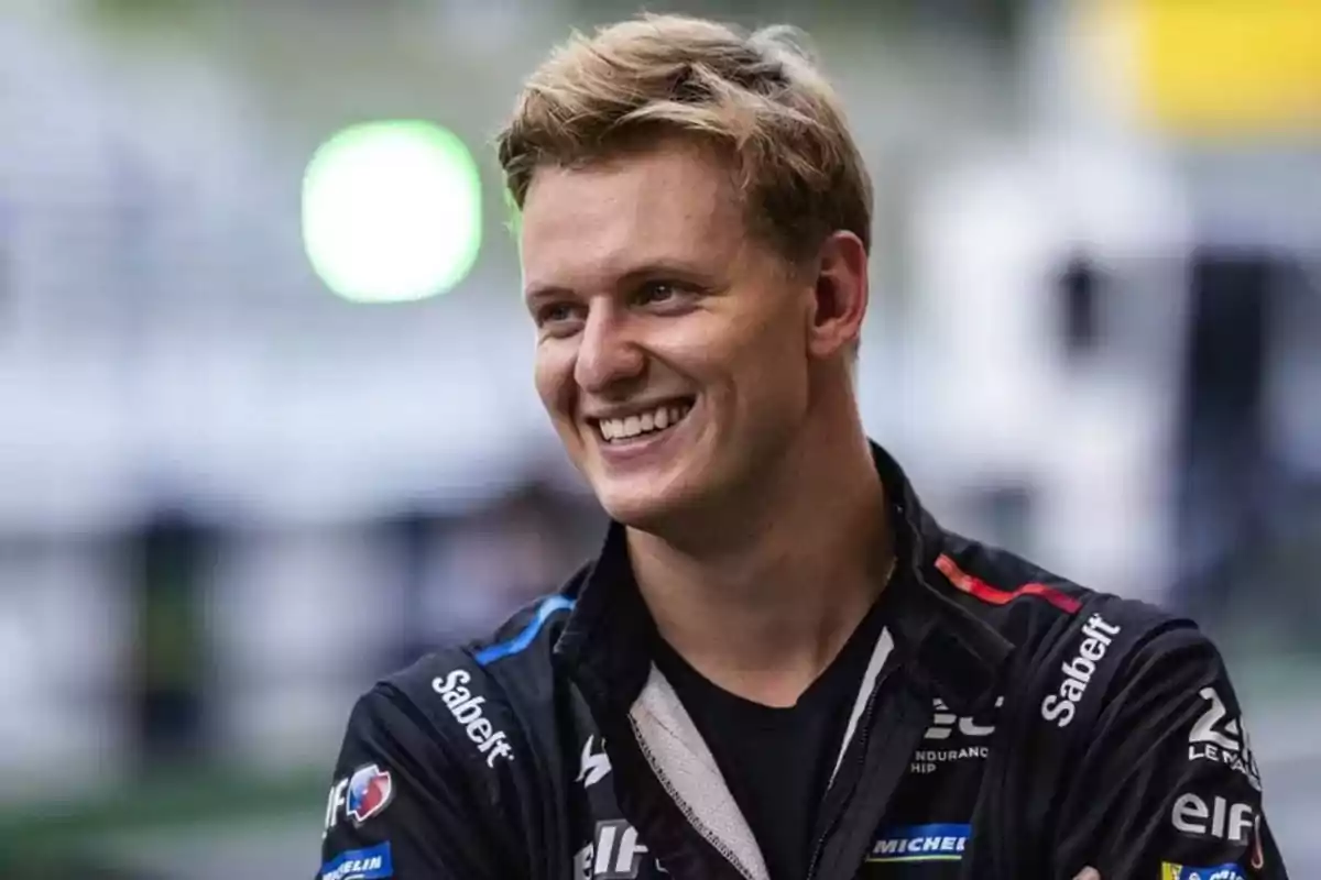 Blond young man in a black sports jacket smiling in a blurred outdoor setting Blond young man in a black sports jacket smiling in a blurred outdoor setting