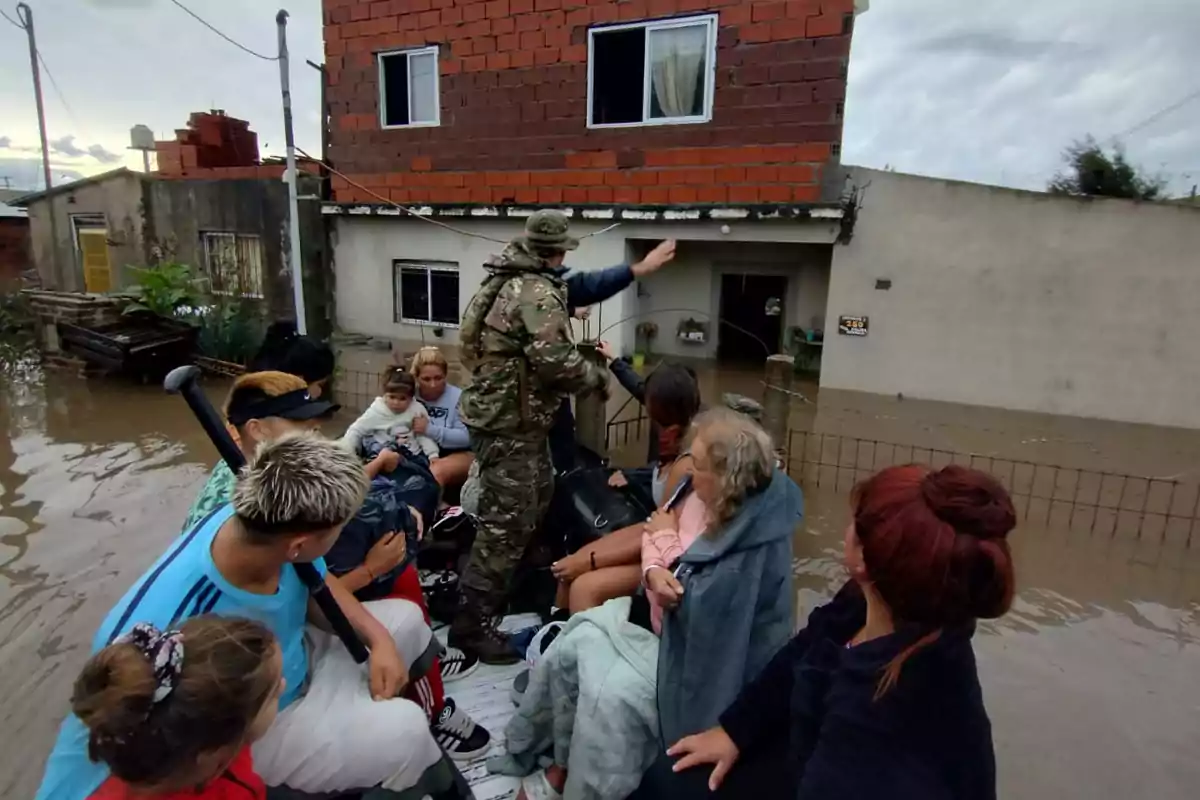 Un grupo de personas es evacuado en un vehículo militar en una zona inundada, mientras un soldado ayuda a coordinar la operación frente a una casa parcialmente sumergida. Un grupo de personas es evacuado en un vehículo militar en una zona inundada, mientras un soldado ayuda a coordinar la operación frente a una casa parcialmente sumergida.