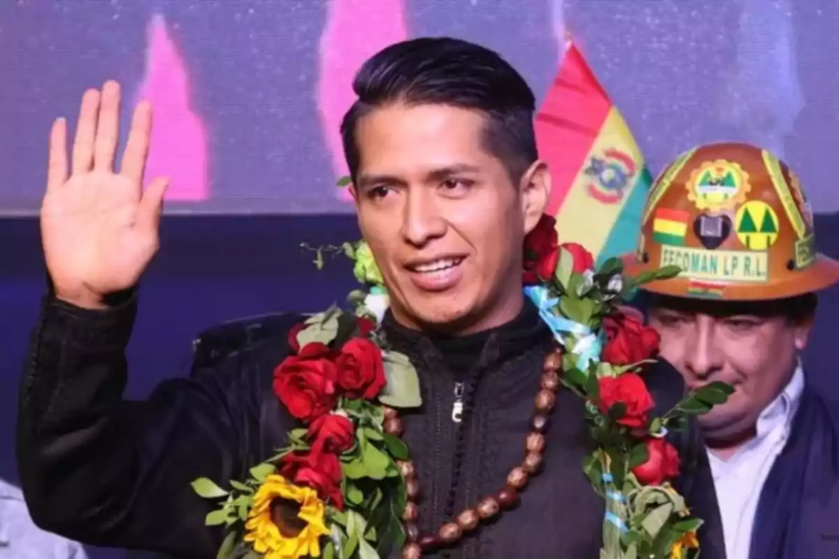 Young man with a flower garland raising his hand and the Bolivian flag in the background