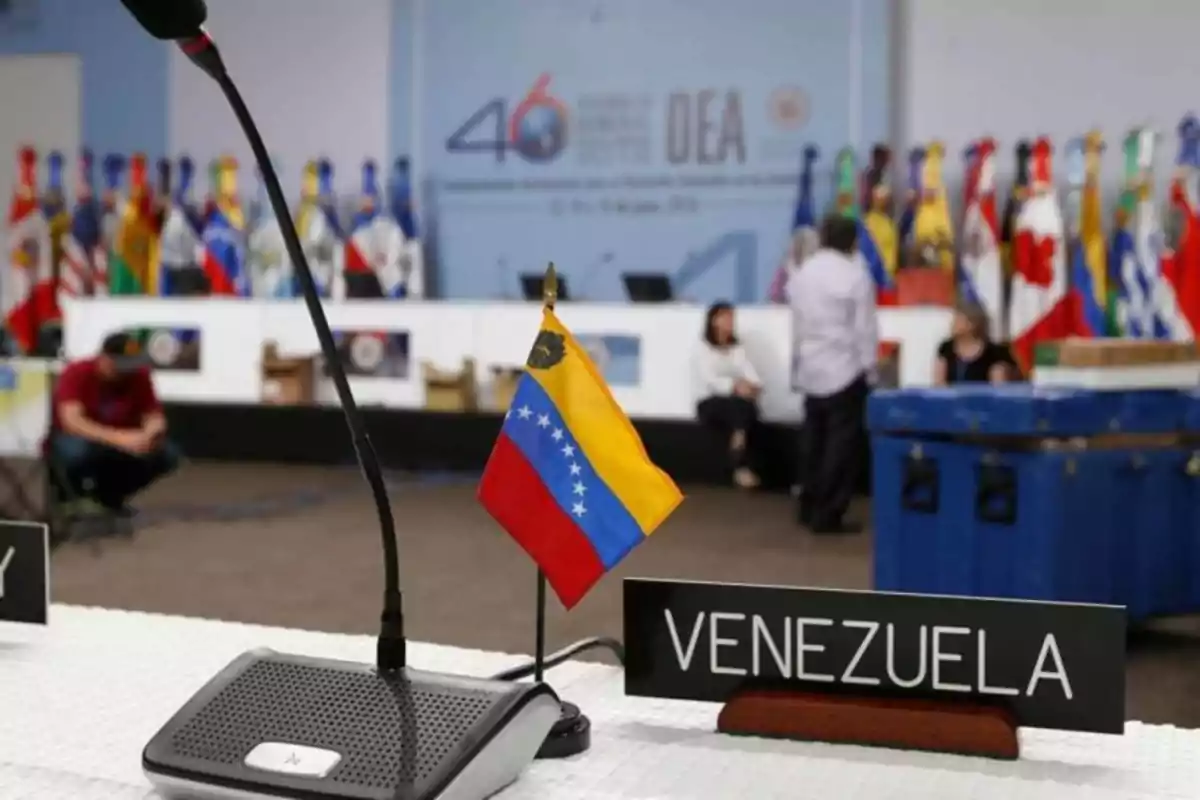 A table with a microphone and a small Venezuelan flag at an international event with several flags of different countries in the background. A table with a microphone and a small Venezuelan flag at an international event with several flags of different countries in the background.