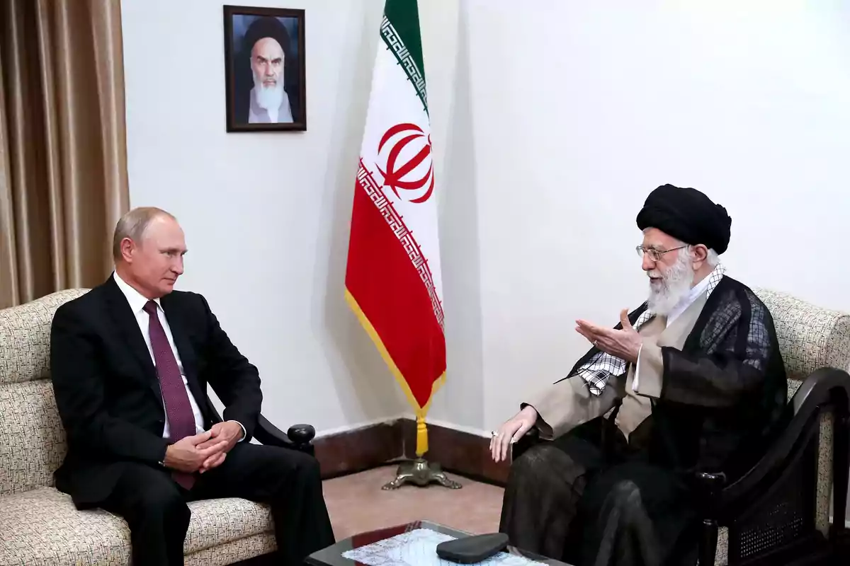 Two men sit and talk in a formal room with an Iranian flag and a portrait on the wall. Two men sit and talk in a formal room with an Iranian flag and a portrait on the wall.