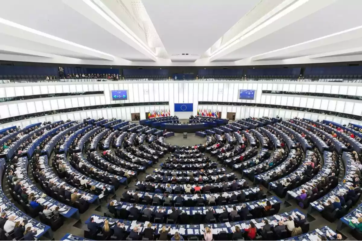 Una vista panorámica del interior de un parlamento con filas de asientos dispuestos en semicírculo y una gran cantidad de personas presentes.