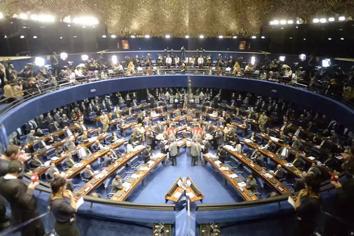 Vista panorámica de un parlamento con numerosos asistentes y periodistas en un recinto circular.