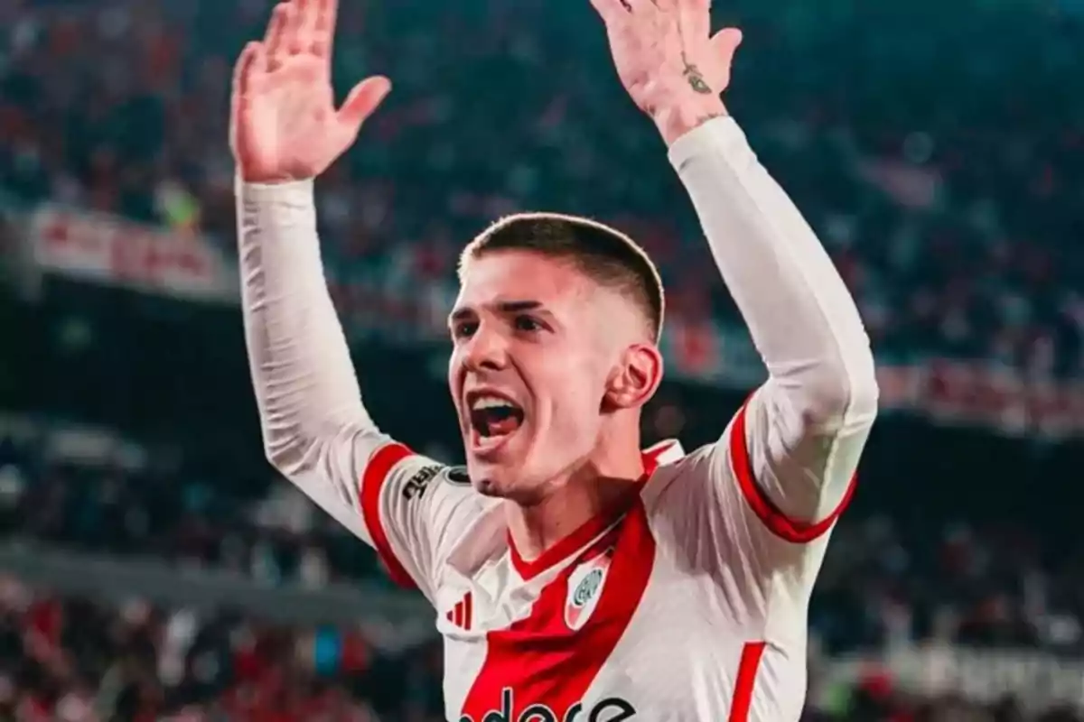 Jugador de fútbol celebrando con los brazos en alto en un estadio.