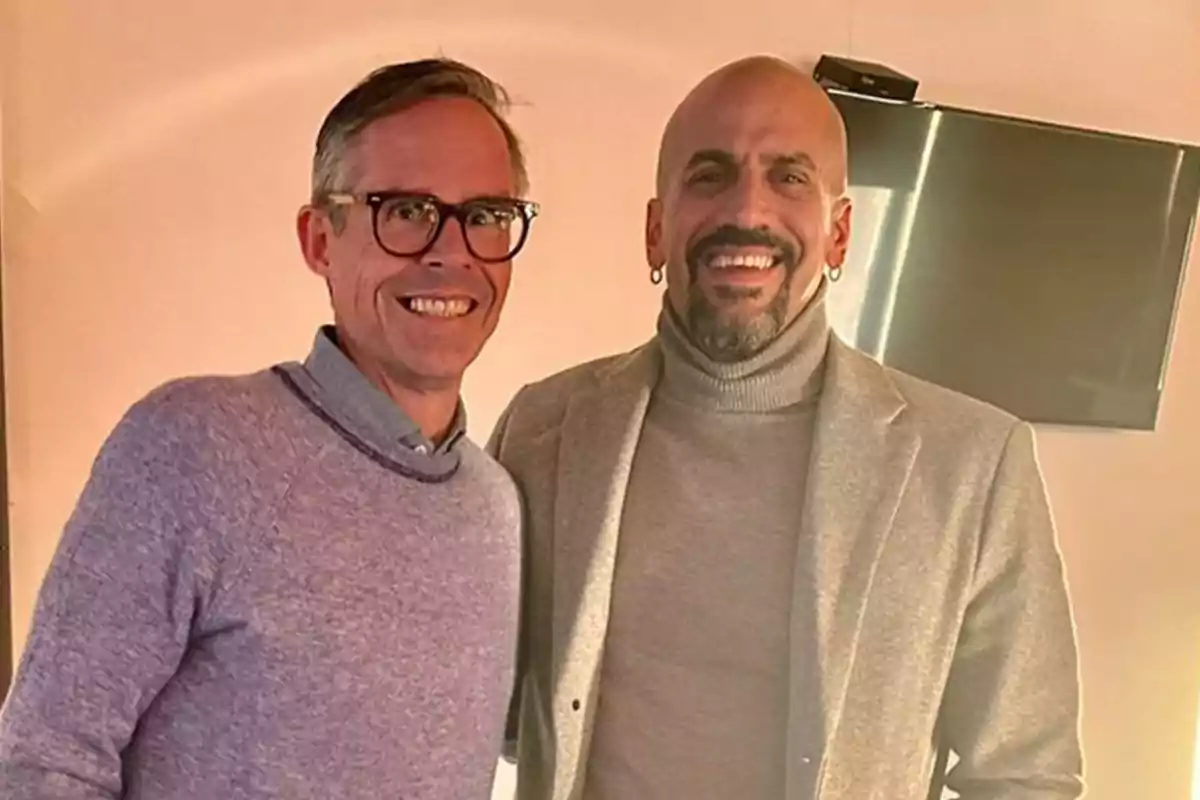 Dos personas sonrientes posan juntas en una habitación con una televisión en la pared.