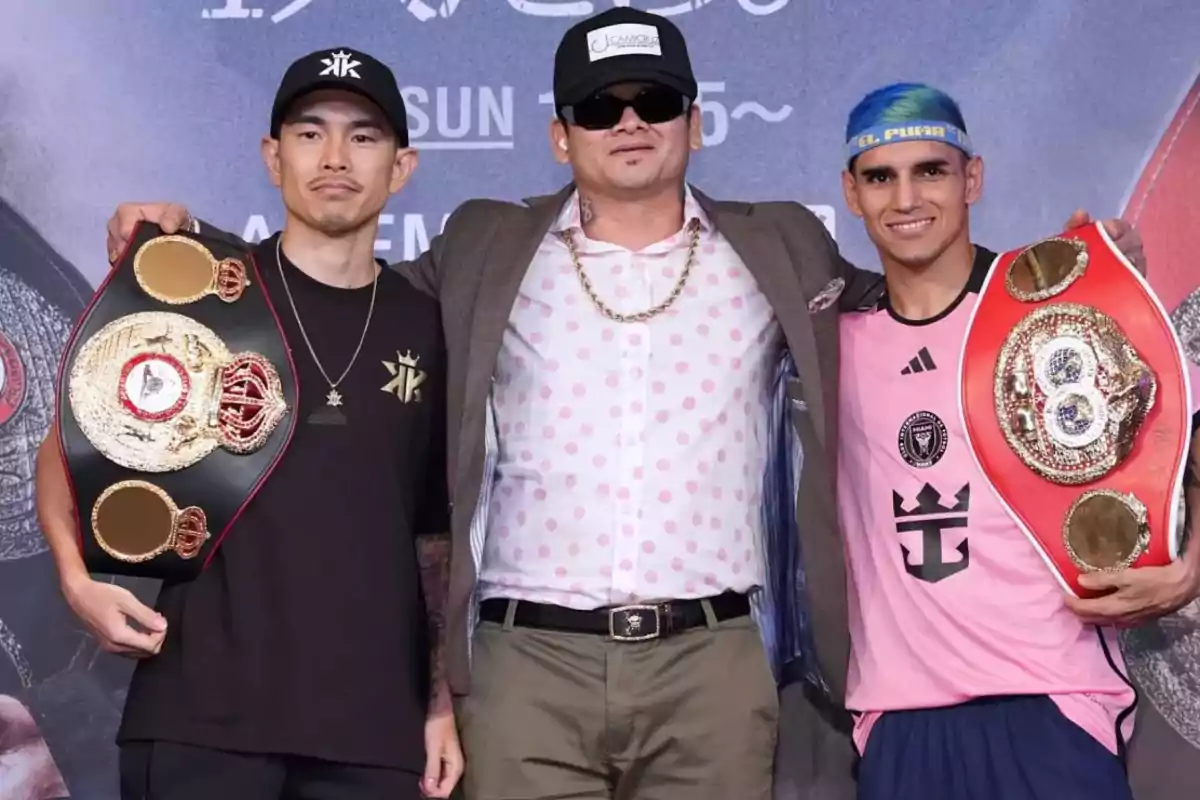 Tres hombres posan juntos, dos de ellos sostienen cinturones de campeonato de boxeo.