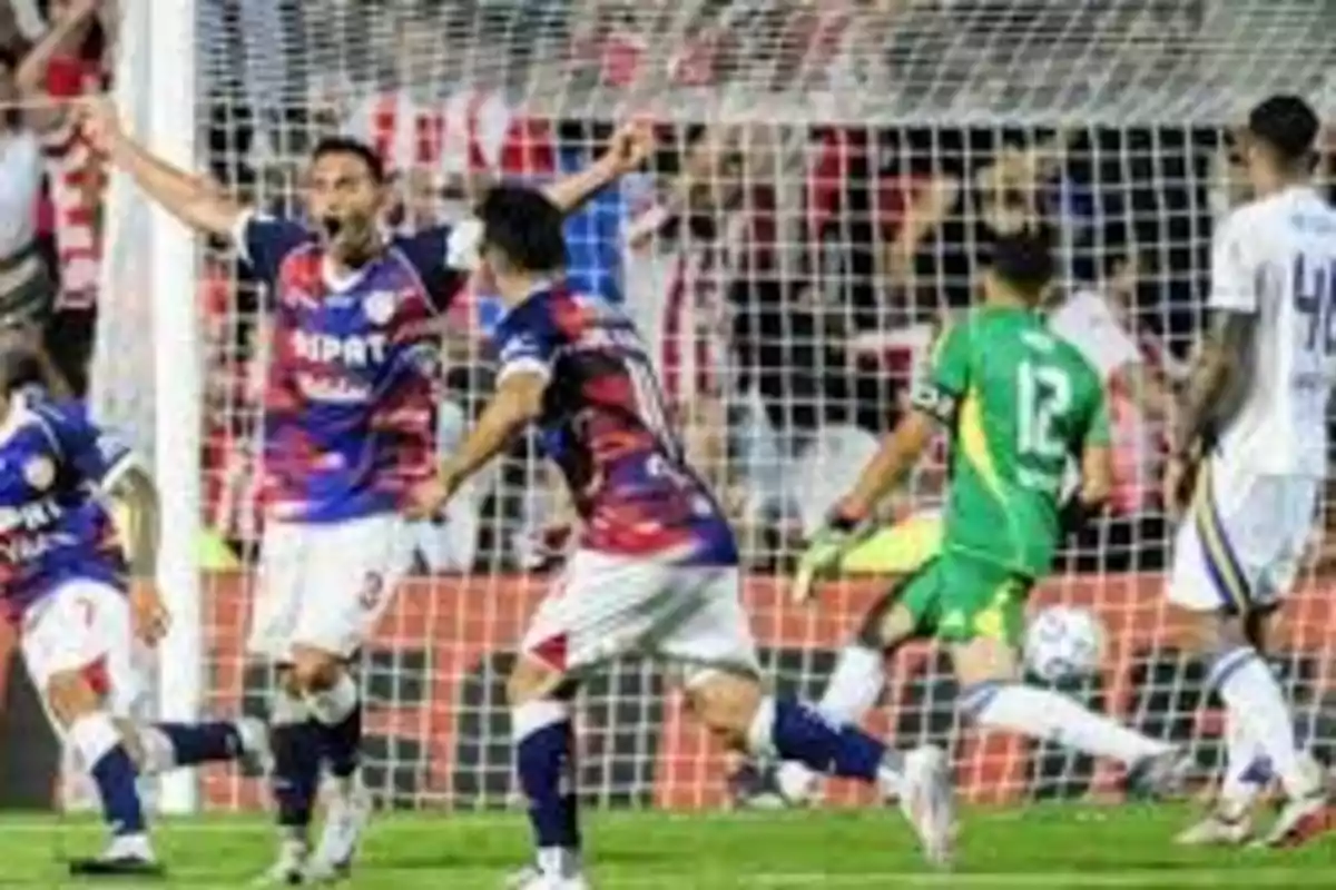Jugadores de fútbol celebrando un gol frente a la portería durante un partido. Jugadores de fútbol celebrando un gol frente a la portería durante un partido.