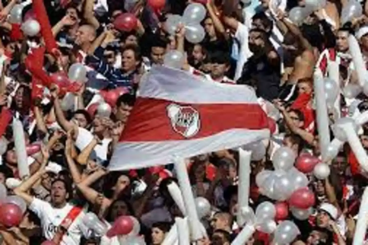 Aficionados celebrando con globos y una bandera en un estadio.