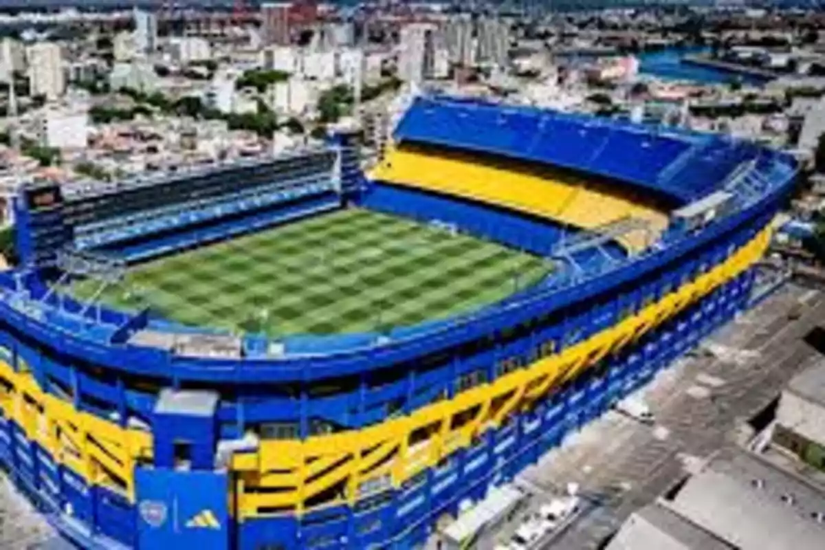 Vista aérea de un estadio de fútbol con gradas azules y amarillas en una ciudad. Vista aérea de un estadio de fútbol con gradas azules y amarillas en una ciudad.