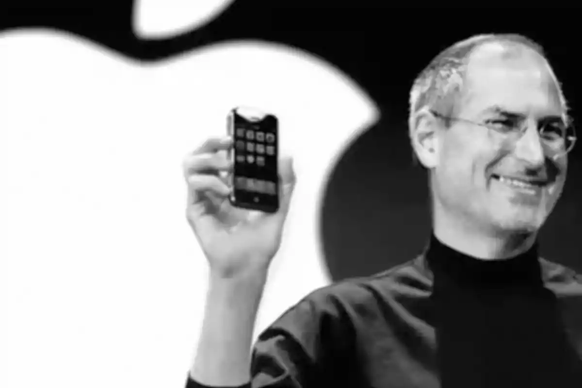 Persona sosteniendo un teléfono móvil frente a un logotipo grande de una manzana. Persona sosteniendo un teléfono móvil frente a un logotipo grande de una manzana.