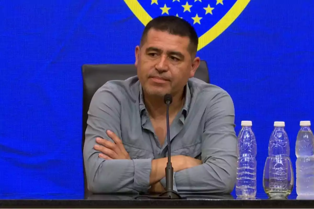 Man sitting at a press conference with a blue background and water bottles on the table. Man sitting at a press conference with a blue background and water bottles on the table.