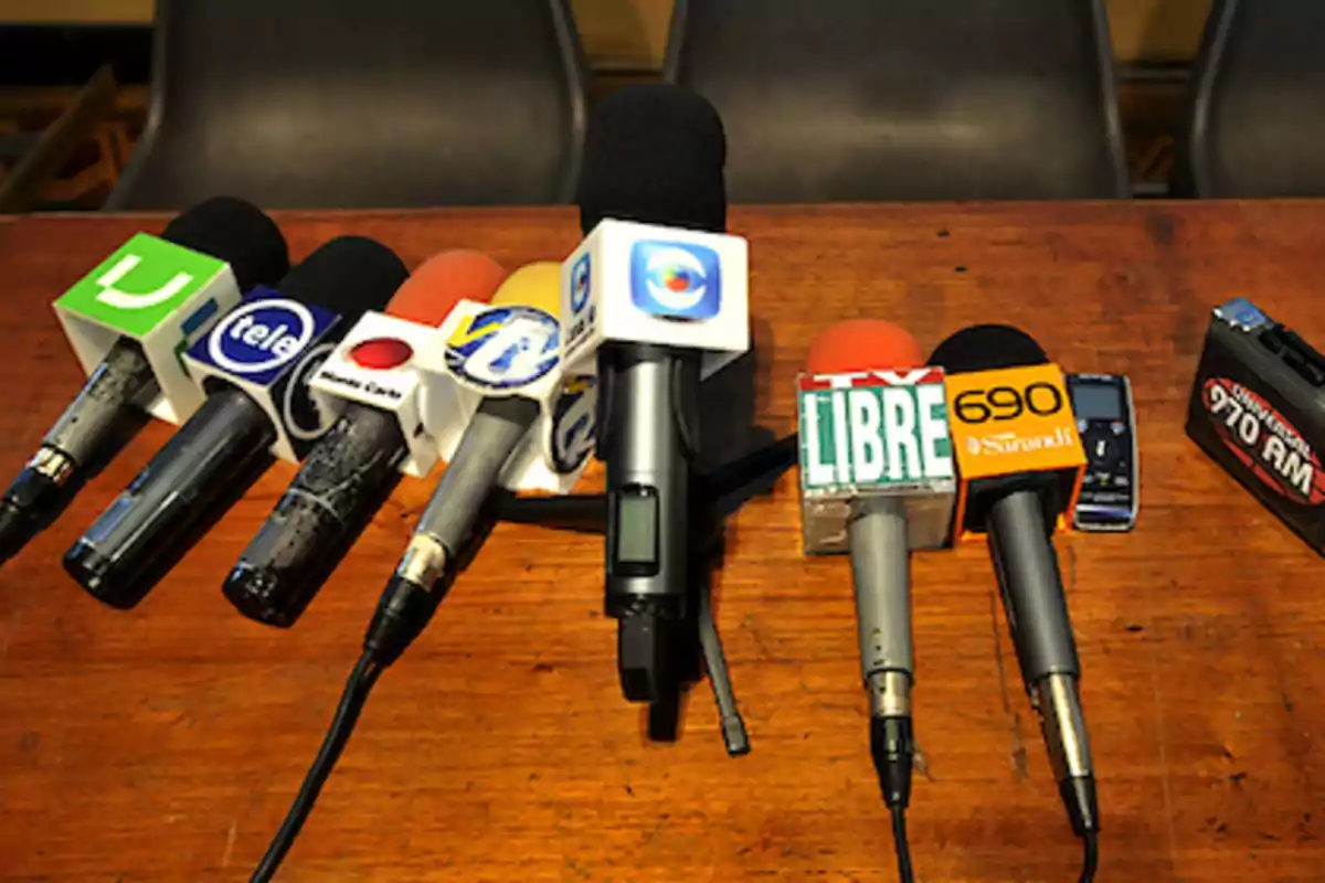 Several microphones from different media outlets on a wooden table. Several microphones from different media outlets on a wooden table.