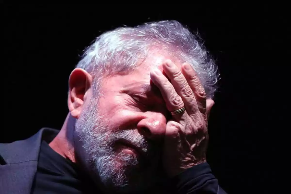 Un hombre con barba y cabello canoso se cubre el rostro con la mano en un gesto de preocupación o cansancio.