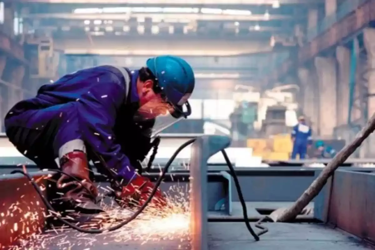 Trabajador con equipo de protección realizando soldadura en una fábrica industrial.