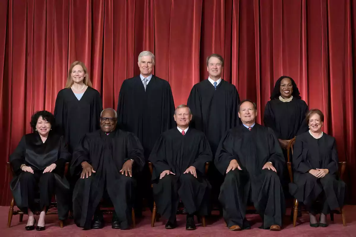 A group of people dressed in black robes posing in front of a red curtain background.