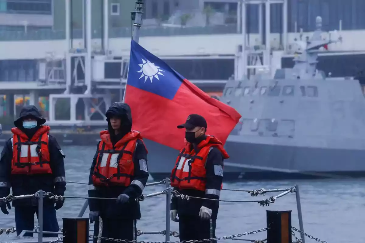 Personas con chalecos salvavidas naranjas en un barco con una bandera ondeando en el fondo.