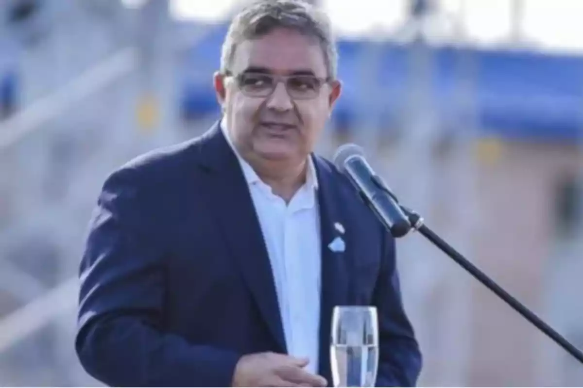 Hombre de traje hablando en un micrófono al aire libre.