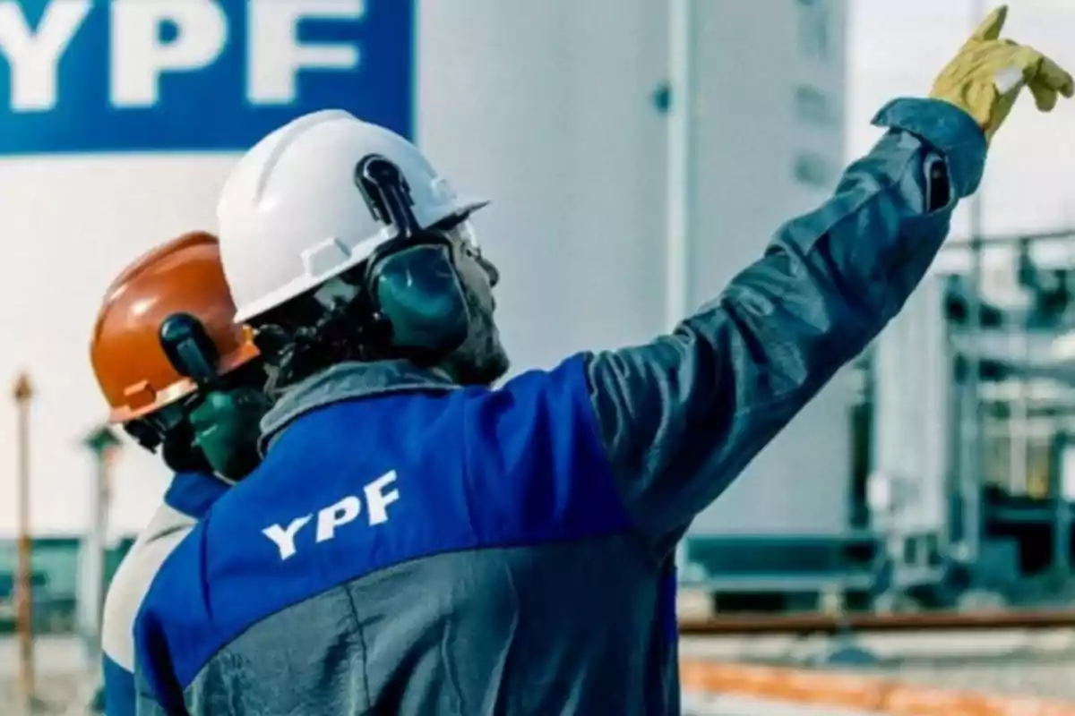 Two workers with helmets and protective gear in an industrial plant, one of them pointing forward.