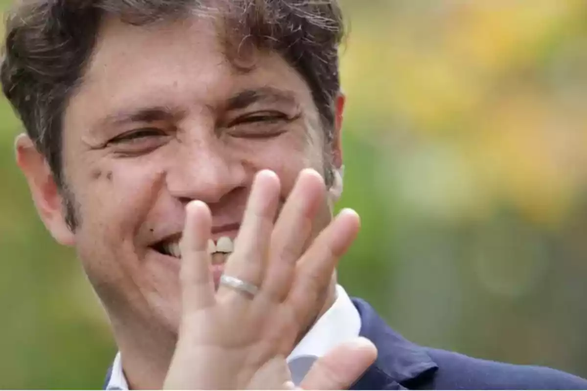 Un hombre sonriendo y levantando la mano frente a su rostro.