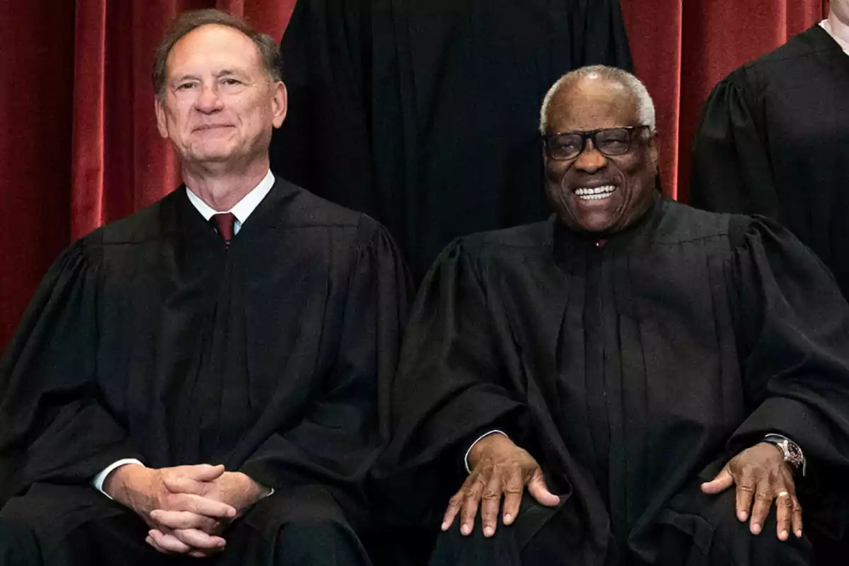 Two people in black robes sitting in front of a red background. Two people in black robes sitting in front of a red background.