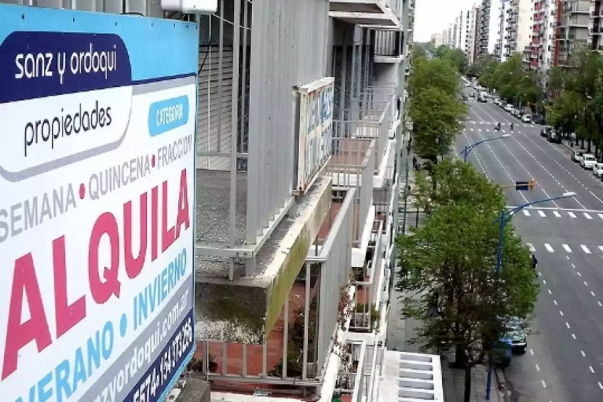 Un cartel de alquiler en un edificio con vista a una avenida arbolada y edificios residenciales.