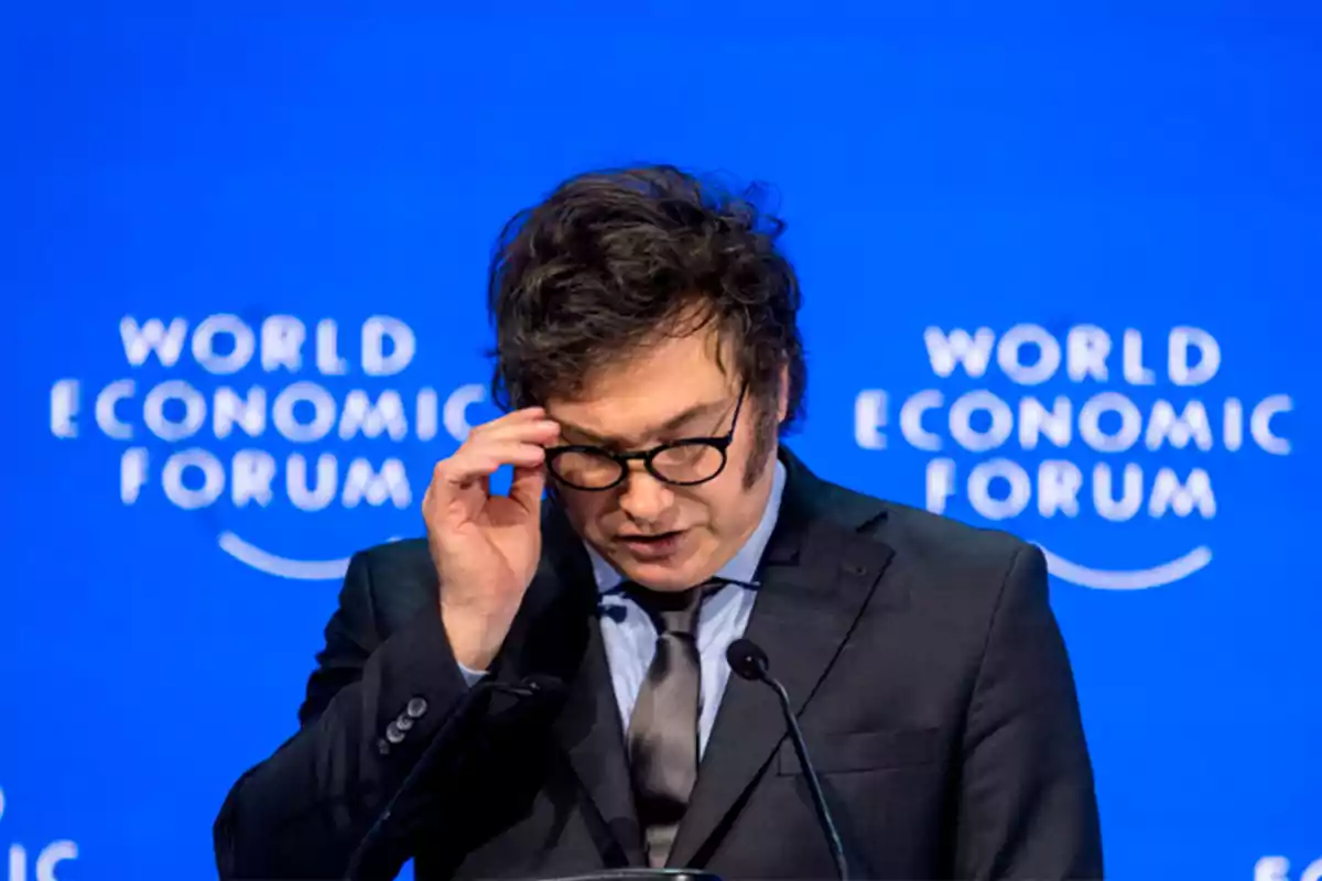 Un hombre con gafas y traje oscuro habla en un podio frente a un fondo azul del World Economic Forum.