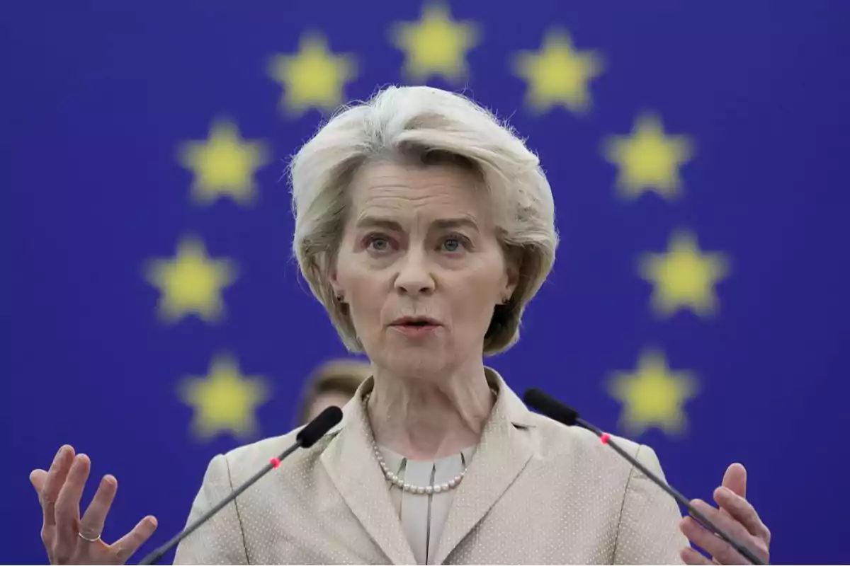 Una persona hablando frente a un fondo con estrellas amarillas sobre un fondo azul. Una persona hablando frente a un fondo con estrellas amarillas sobre un fondo azul.