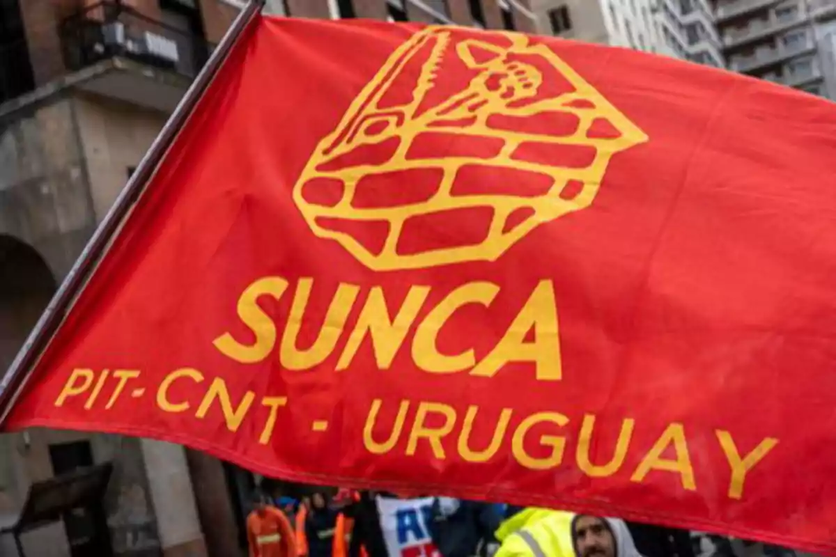Bandera roja con el logo y las letras amarillas de SUNCA PIT-CNT Uruguay ondeando en una manifestación urbana