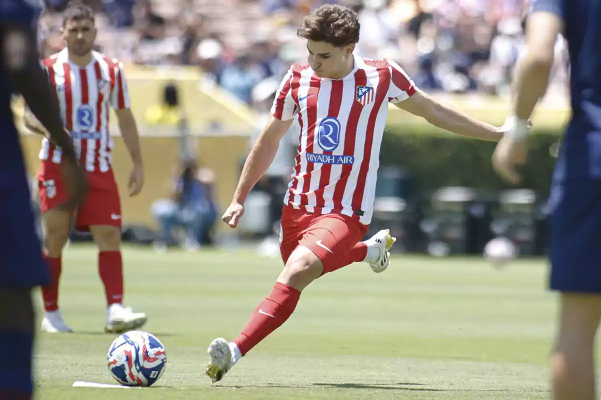 Atlético de Madrid player in a red and white uniform kicking a ball during a soccer match in an outdoor stadium Atlético de Madrid player in a red and white uniform kicking a ball during a soccer match in an outdoor stadium