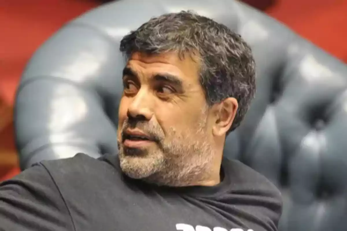 Gray-haired, bearded man sitting in a blue armchair looking to the side