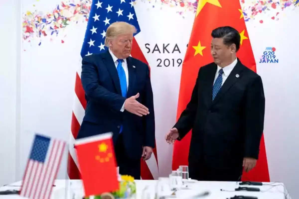 Two world leaders stand in front of the flags of the United States and China during a meeting at the G20 in Japan in 2019, one of them reaching out to shake hands with the other.