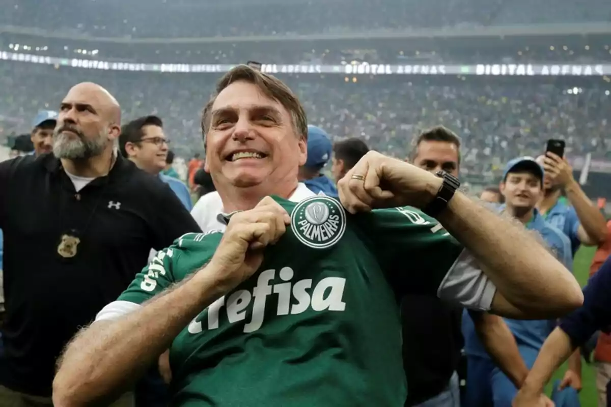 Hombre sonriente mostrando el escudo del club Palmeiras en su camiseta dentro de un estadio lleno de aficionados Hombre sonriente mostrando el escudo del club Palmeiras en su camiseta dentro de un estadio lleno de aficionados
