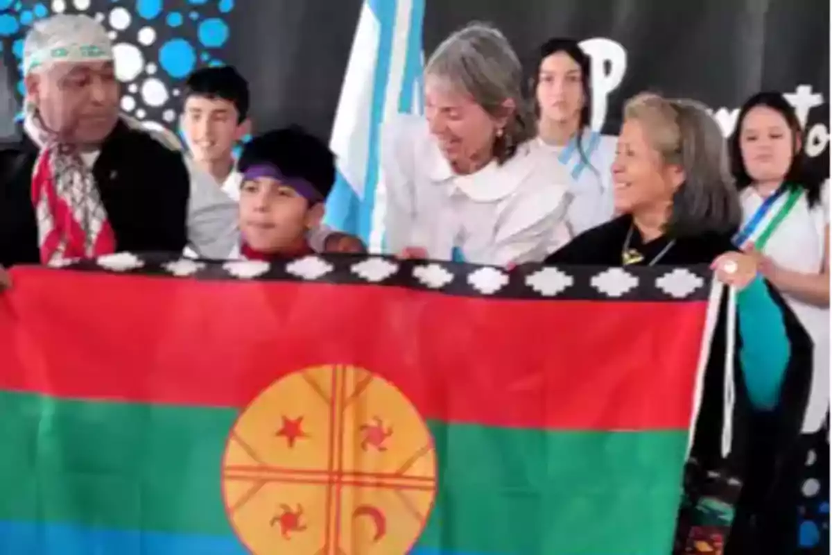 Personas sosteniendo una bandera mapuche en un evento escolar