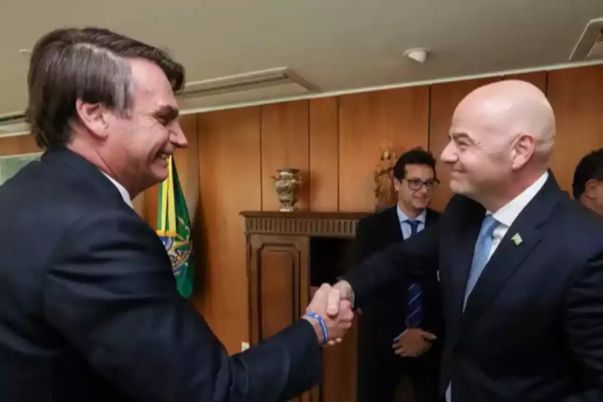 Dos hombres de traje se dan la mano y sonríen en una oficina con una bandera de Brasil al fondo